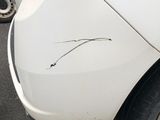the rear end of a white car with a dent in it ' s bumper