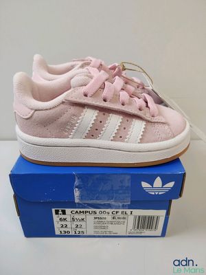 une paire de baskets Adidas roses et blanches posées sur une boîte bleue