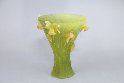 un vase vert contenant des fleurs jaunes, posé sur une surface blanche