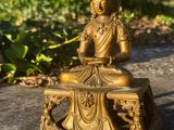 brass statue of a buddha sitting on a bench in a garden