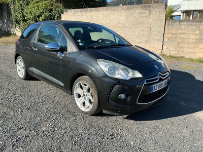 La petite voiture noire est garée sur le gravier, près d'un mur de briques.