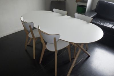 une table blanche avec quatre chaises et un canapé noir en arrière-plan