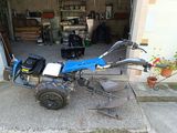 an image of a small blue tractor parked in front of a garage