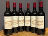 six bottles of red wine are lined up on a wooden barrel