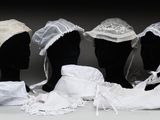 trois mannequins coiffés de chapeaux et vêtus de tissus blancs, posés sur une table