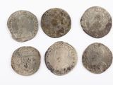 six silver coins of different sizes and shapes on a white surface