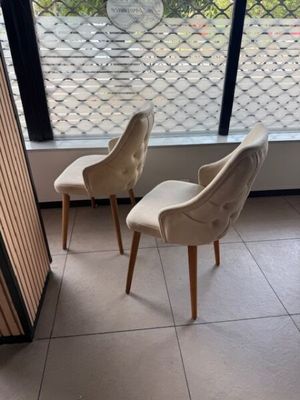 deux chaises beiges placées devant une fenêtre où se trouve un vase de fleurs