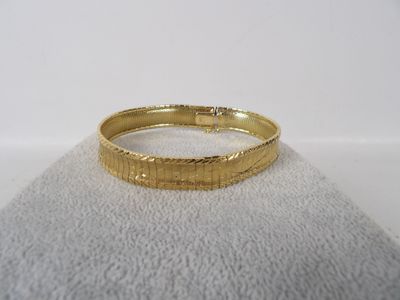 gros plan d'un bracelet en or sur une surface blanche