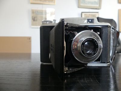 un appareil photo noir posé sur une table, avec des photos accrochées au mur derrière lui