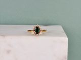 un gros plan d'une bague sertie d'une émeraude verte et de diamants, posée sur un bloc de marbre blanc