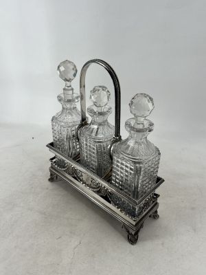 une carafe en verre plaquée argent, accompagnée de trois bouteilles posées sur un socle
