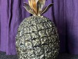un petit ananas posé sur une table, avec un rideau violet en arrière-plan