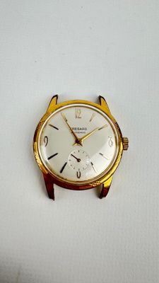 une montre en or avec un cadran blanc posée sur une surface blanche