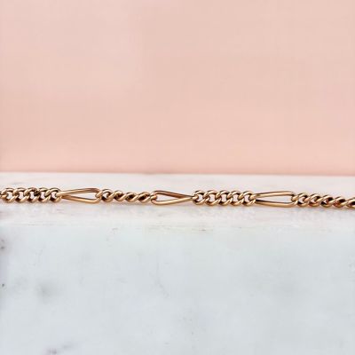 un gros plan d'un bracelet à chaîne en or posé sur une surface en marbre