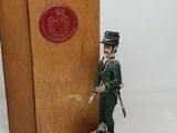 figurine of a soldier in a green uniform standing next to a wooden box