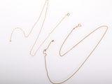 three gold necklaces and a chain on a white surface