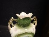 a green vase with a flower on it on a black surface