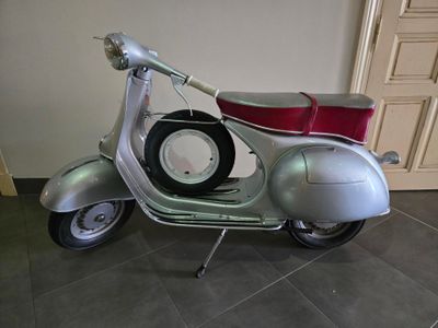 une trottinette argentée avec un siège rouge posé par terre