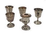 Plusieurs gobelets et tasses en argent sont alignés sur une surface blanche