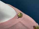 a pink sweater with a gold button on it