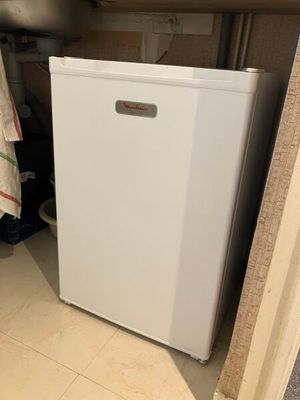 un petit réfrigérateur blanc dans le coin d'une pièce