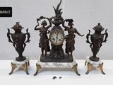trois statues posées sur une table, avec une horloge au milieu
