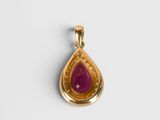 a close up of a gold pendant with a red stone