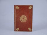 an old red book with gold trim sitting on top of a white surface