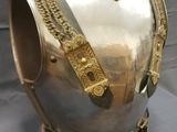 an antique silver and gold vase with chain handles on a table