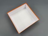 une boîte carrée orange et blanche avec un couvercle, posée sur une surface grise