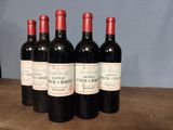 four bottles of red wine are lined up on a wooden table