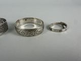 three silver bracelets and a ring on a white surface