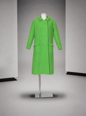 une photo d'un manteau vert posé sur un présentoir à mannequin dans une pièce