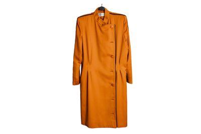 Un manteau orange est suspendu à un cintre accroché à un mur blanc.