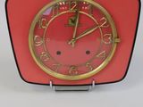 une horloge rouge au cadran doré, à côté d'une clé