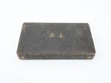 an old black book with gold writing on it sitting on a white surface
