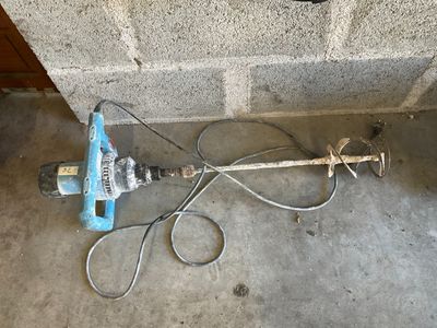 a blue and white drill on the ground next to a brick wall