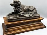 une statue en bronze représentant un chien couché sur un socle en bois