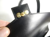 a hand holding a black purse with gold buttons