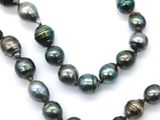 a close up of a strand of black pearls on a white surface