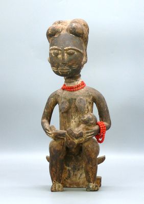 une statue en bois représentant une femme tenant un chat qui porte un collier de perles rouges