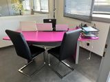 une table rose avec des chaises noires et un ordinateur portable posé dessus