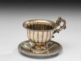 une tasse et une soucoupe en argent posées sur une soucoupe, elle-même posée sur une autre soucoupe