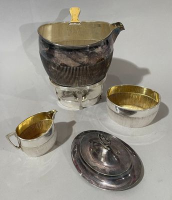 une théière en argent et deux tasses en argent posées sur une table blanche