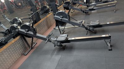 row of rowing machines in a gym with mirrors on the wall