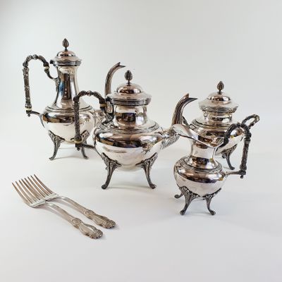 a silver tea set on a table with a fork and knife