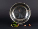 an antique silver plate with beading and a plant on a black background