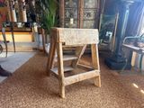 a wooden stool sitting in a living room next to a potted plant