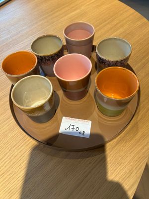 six tasses de couleurs différentes posées sur une assiette, sur une table