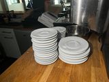several white plates are stacked on a wooden counter in a kitchen